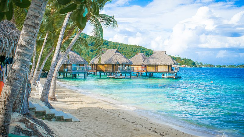 Bora Bora Tahitan French Polynesia beach, palms and thatch-roofed dwellings over azure blue seas