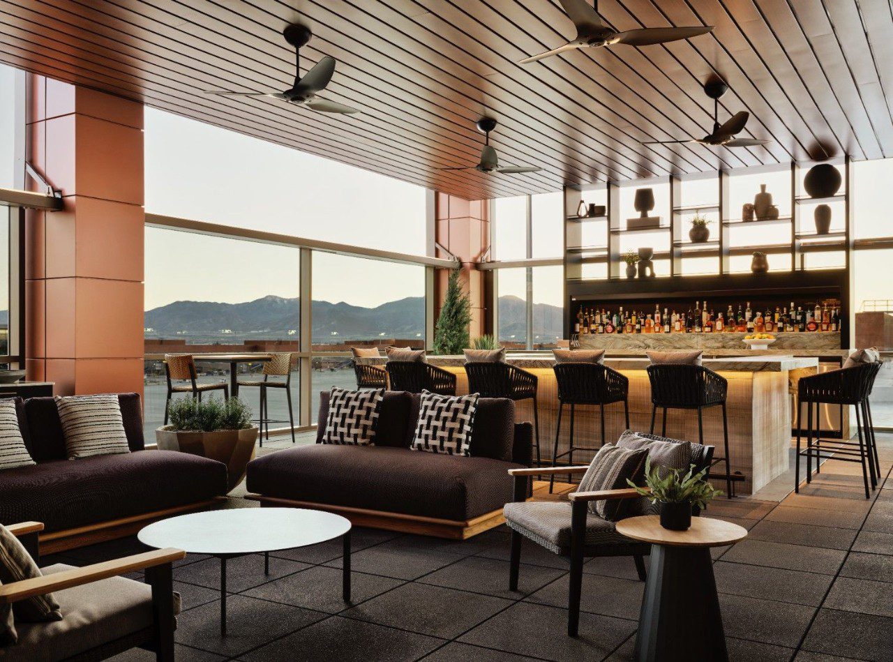 One of two bars at the American Express Centurion Lounge at Salt Lake City International airport. A bar, high-top seating, couch seating, and floor-to-ceiling windows with views of mountains are pictured.